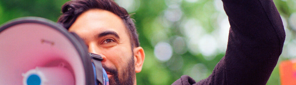 Zohran Mamdani speaking into a bullhorn at Fort Greene Park in Brooklyn on 5/24/2025