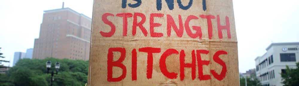 Sign at the Newark No Kings rally written in red and black on cardboard that reads "CRUELTY IS NOT STRENGTH BITCHES."