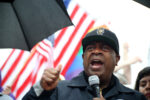 Ras Baraka addressing the crowd at the Newark No Kings rally in the rain, US and Pride flag flying behind him