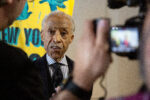 Rev. Al Sharpton getting interviewed after the press conference. We're looking at him over the shoulders of the interviewer on the left and a videographer on the right - screen of the video camera blurry in the foreground.