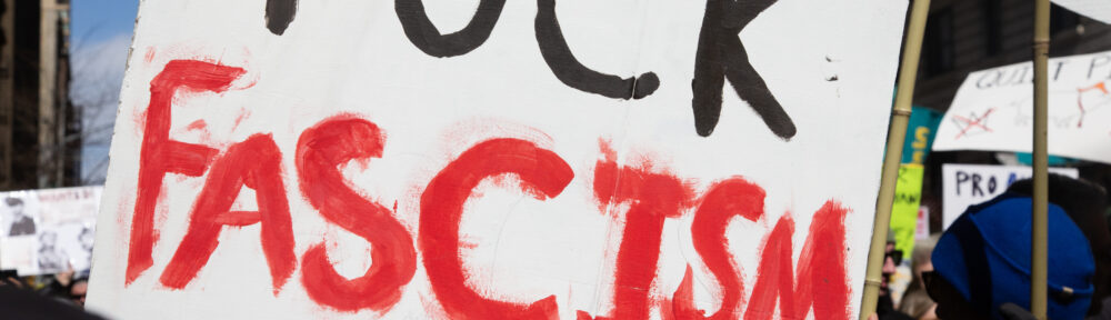 Person holding up a sign that says FUCK FASCISM in hand painted black and red.