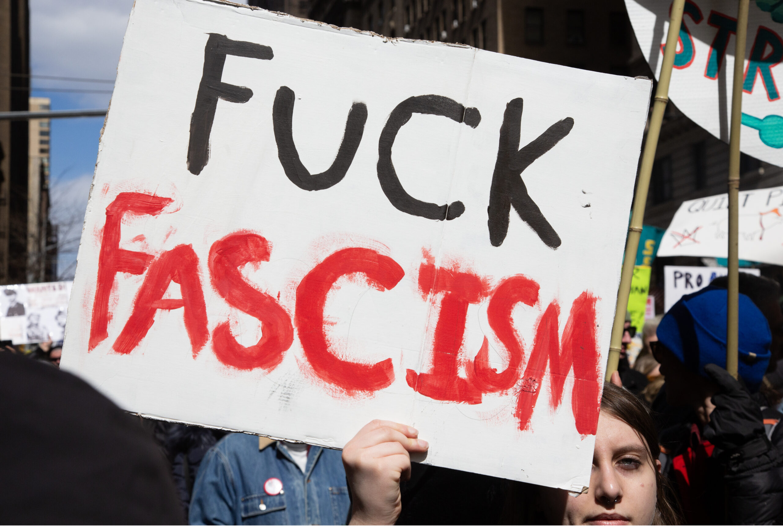 Person holding up a sign that says FUCK FASCISM in hand painted black and red.