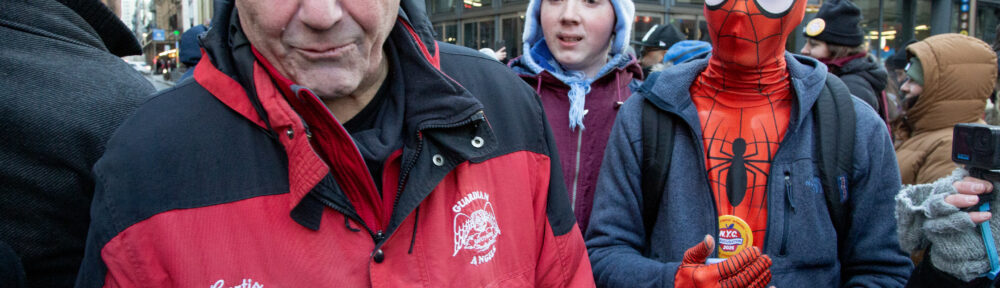 Curtis Sliwa smiles at the camera at Fulton and Broadway after the inauguration. A person dressed as Spider-Man stands behind him.