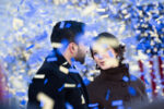 Zohran Mamdani and Rama Duwaji surrounded by falling confetti during the inauguration. They're gazing at each other. She's smiling. Face partly covered by glowy falling confetti.