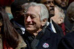 Robert De Niro smiles while looking off to the side while marching in No Kings Manhattan. He's wearing a button that says "I [heart] IMMIGRANT NY"